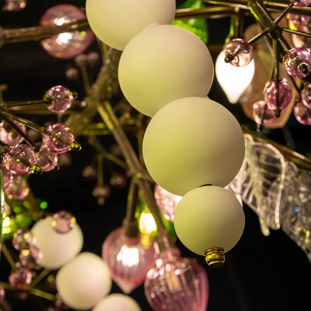Close-up of the Pandora Chandelier showing clusters of lit opal white glass globes among pink glass elements on brass stems