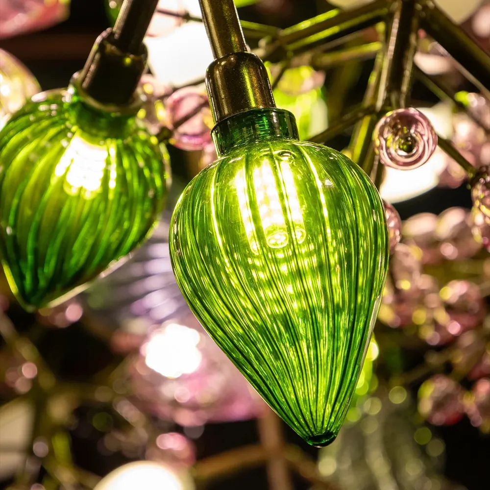 Close-up of a lit green ribbed glass pendant on the Pandora Chandelier, glowing from an internal lamp